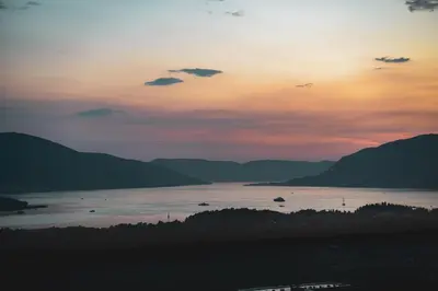 a sunset over a body of water with mountains at Royal Blue Resort & Residences in Tivat