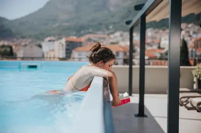 a woman in a swimming pool with a book at Hotel Diplomat by Aycon in Budva