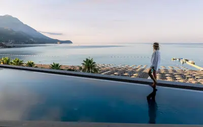 a woman walking on the edge of a swimming pool overlooking the ocean at Sea Star Budva in Budva