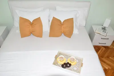 a white bed with orange pillows and a tray of scissors at Apartment City View in Kotor