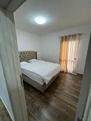 a bedroom with a bed with white sheets and wooden floors at Cezar Apartment 3 in Podgorica