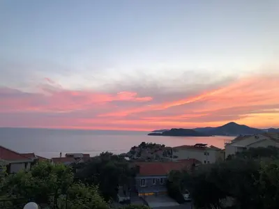 a sunset over the ocean with houses and a city at Apartment Skada in Sveti Stefan
