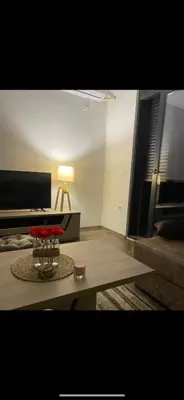 a living room with a table and a bed and a lamp at Glamur Apartman - Ulcinj in Ulcinj
