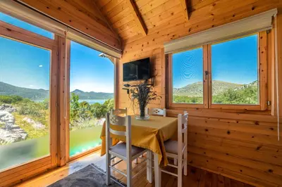 a dining room with a table and chairs and windows at Boljesestre Lake retreat in Golubovci