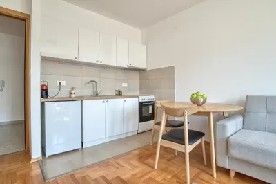 a kitchen with white cabinets and a table and a couch at Sigma apartment in Budva