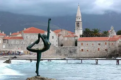 a statue of a woman in the water in front of a city at Tara Two Bedroom Apartment - Budva in Budva