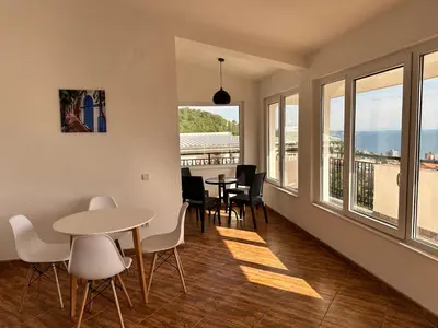 a living room with a table and chairs and windows at Best View Apartment in Sutomore
