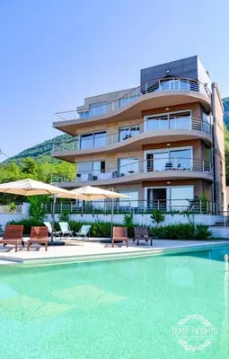 a building with a swimming pool with chairs and umbrellas at Golden Suit Tivat Heights-Pool & Seaview C1 in Kavač