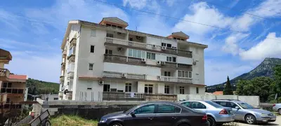 a tall white building with cars parked in front of it at Sutomore apartman in Sutomore