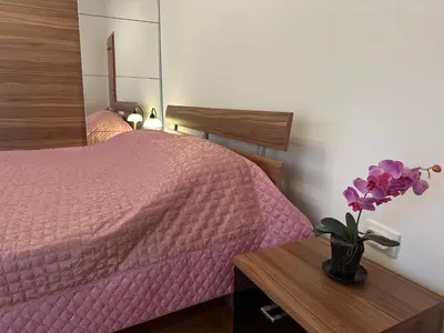 a bedroom with a pink bed and a vase with purple flowers at Apartments Comfort Petrovac in Petrovac na Moru