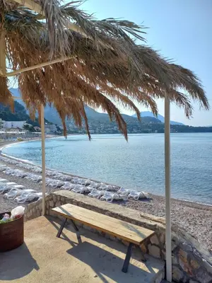 a wooden bench under a straw umbrella on a beach at STELLA di mare in Sutomore
