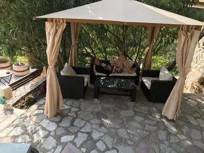 two women sitting on couches under an umbrella at Семейный комплекс для отдыха in Pečurice