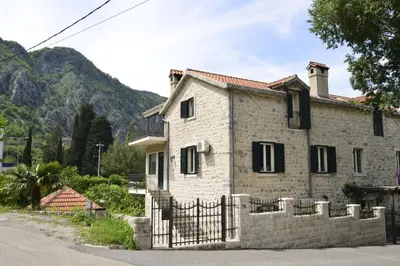 a stone house with a fence and mountains in the background at Villa Andrea Apartments with parking in Kotor