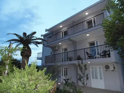 a large white building with a palm tree in front of it at Apartments Macaso in Bar
