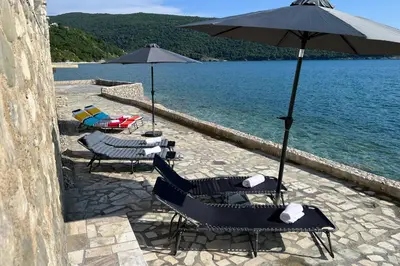 a group of chairs and umbrellas next to the water at Sea Breeze Apartment in Kruče