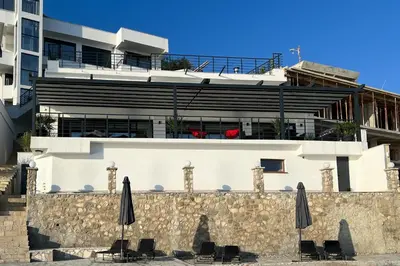 a white building with chairs and umbrellas in front of it at Sea Wave Apartment in Kruče