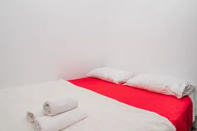 a white bed with red and white sheets and pillows at Apartman Glendza in Ulcinj