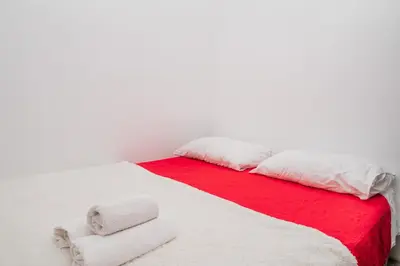 a white bed with red and white blankets and pillows at Glendza Apartman in Ulcinj