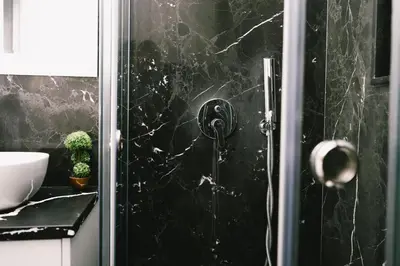 a bathroom with a shower with a black marble wall at Apartments Moon White Lux in Ulcinj