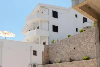a white building with balconies and a stone wall at Higo Apartments in Ulcinj