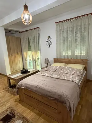 a bedroom with a bed and a table and windows at Kropa apartman in Podgorica