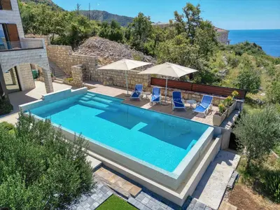 a swimming pool with two blue chairs and an ocean at Vila Aria vista in Petrovac na Moru
