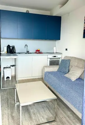 a living room with a couch and a kitchen with blue cabinets at Miločer Apartman Beograd in Pržno