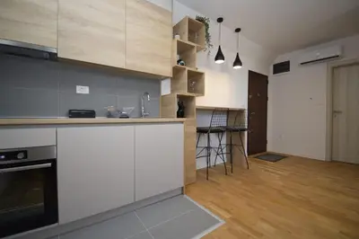 a kitchen with white cabinets and a wooden floor at Studio apartment Art Zone II in Podgorica