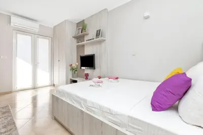 a white bedroom with a large bed with purple pillows at Apartments Marilu in Kotor
