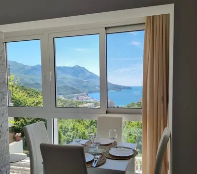 a dining room with a table and a large window at Apartman Marija sa ličnim đakuzijem in Becici
