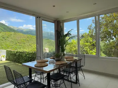 a dining room with a table and chairs and windows at Apartman Marija sa ličnim đakuzijem in Becici