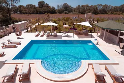 a pool with chairs and umbrellas on a patio at Villa 100 Palme in Ulcinj