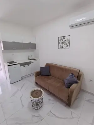 a living room with a brown couch and a kitchen at lux apartmani Porte Nouva in Sutomore