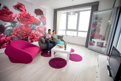 two people sitting in a living room with a wall of flowers at Apart Hotel Sea Fort in Sutomore