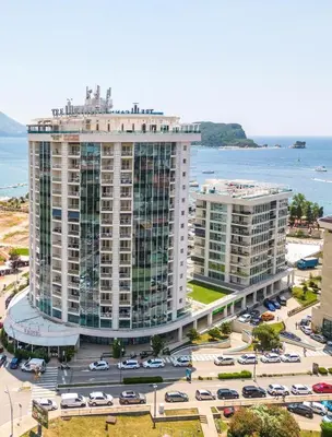 a large building with cars parked in a parking lot at Two rooms in Tre canne hotel in Budva