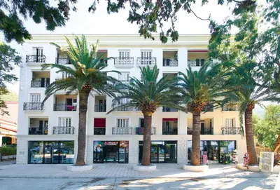 a white building with palm trees in front of it at Apartments Dangubic in Petrovac na Moru
