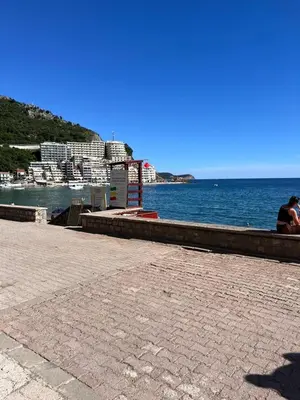 a person sitting on a bench next to the water at Montenegro at the Green Stone beach in Budva