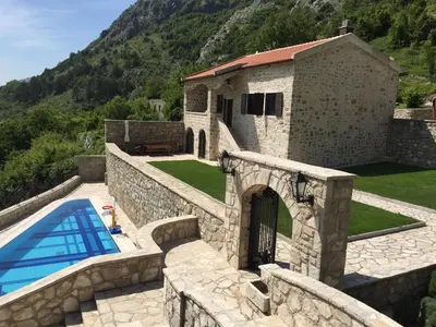 a stone house with a swimming pool next to a mountain at Blake's Villa in Budva