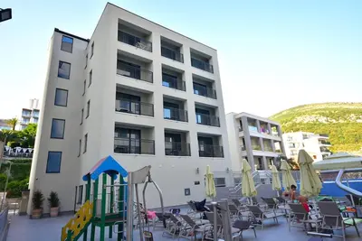 a large white building with a playground in front of it at Brand New ! Seaside Apt with Poolview & Parking in Budva