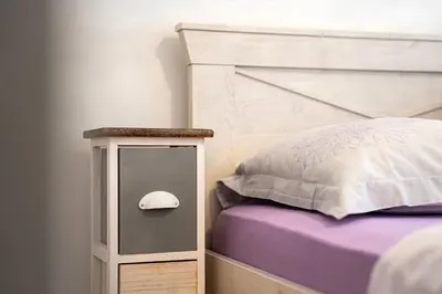 a bed with a white headboard and a table with a pillow at Spacious two bedroom in Podgorica