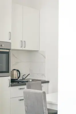 a kitchen with white cabinets and a sink and a chair at One-Bedroom Apartment in the Center of Budva on a Quiet Street 5 Minutes to the Beach in Budva