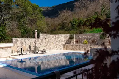 a swimming pool with two chairs and a stone wall at Majestic Apartment in Tivat