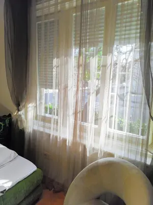 a window with white curtains and a chair in front of it at Studio apartment CENTER in Podgorica