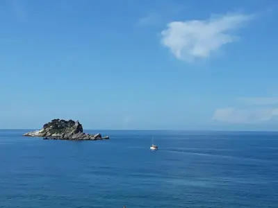 a boat in the ocean with a small island at Apartments Teodora Obala in Petrovac na Moru