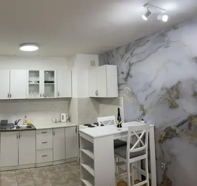 a kitchen with white cabinets and a marble wall at Royal in Podgorica