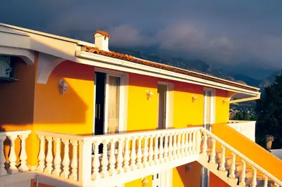a yellow house with a white railing on a balcony at Vila Bronhi in Sutomore