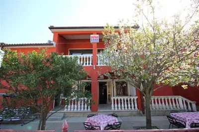 a red building with tables and trees in front of it at Apartmani Dresic in Sutomore