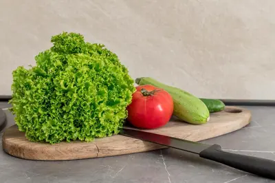 a cutting board with a lettuce and a tomato and a knife at Apartment Petar 1 in Kotor