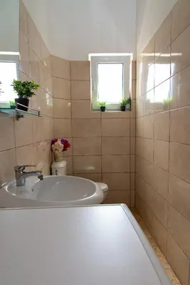 a bathroom with a sink and a toilet and two windows at Vila Apartmani Astoria in Podgorica