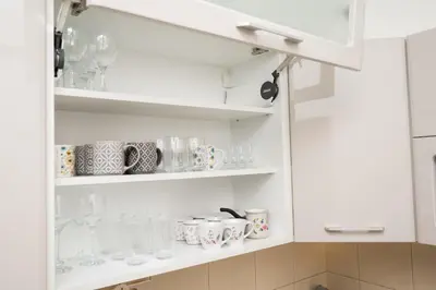 a white cupboard filled with glasses and mugs at Apartman Klara Podgorica in Podgorica